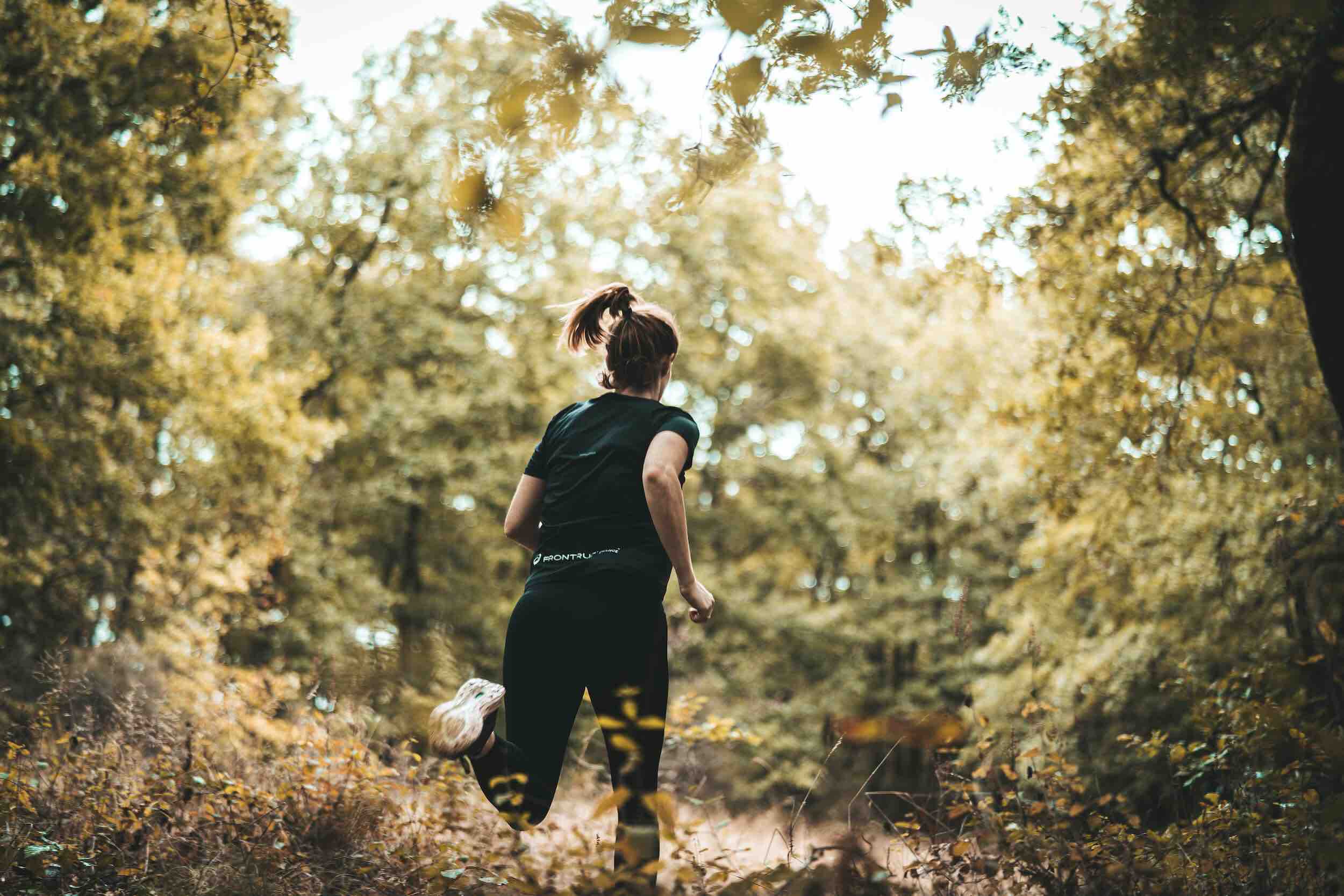 Sportive en train de courir dans une forêt, de dos