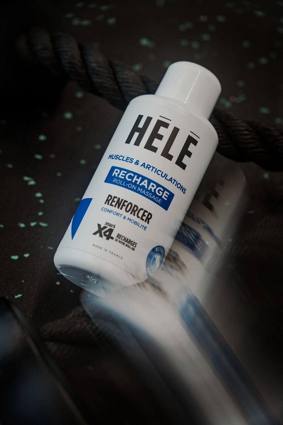 Recharge roll-on massage Renforcer HELE Sport posée sur un tapis de sol sombre, à côté d’une corde